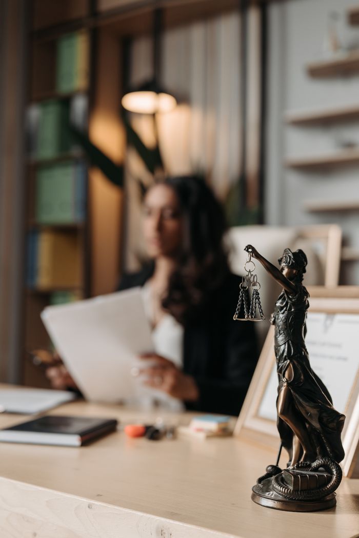 Services Close-up of a justice figurine on desk with blurred female lawyer in office setting.